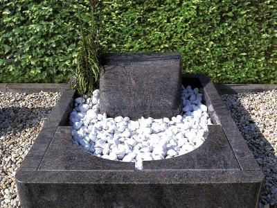 Urnengrab aus poliertem Granit mit abgerundeter Einfassung, formschönen Abdeckplatten und liegendem Grabstein in Kissenform