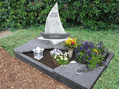 Urnengrab mit Einfassung und Abdeckplatten in Wellenform mit mehrteiligem Grabstein in Schiffform aus bicolor Granit