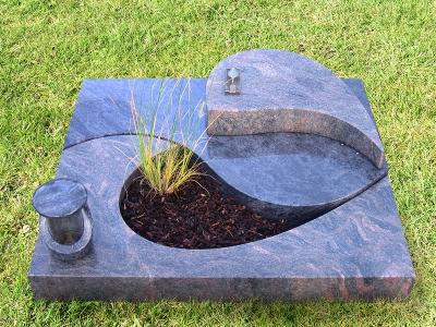 Modernes Urnengrab aus zwei Granitsorten mit formschönem Teilausschnitt und dazu passendem Liegestein sowie Grablampe aus Stein